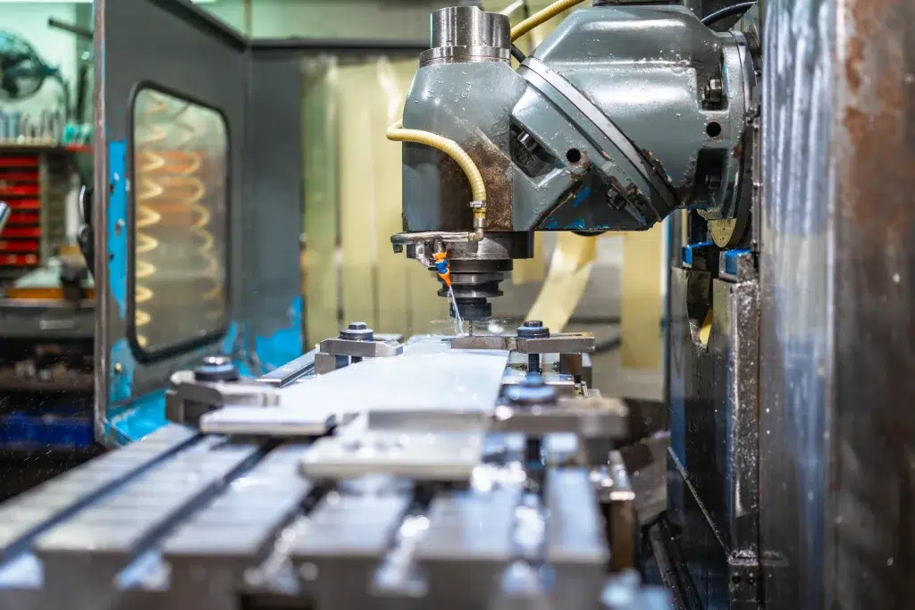 Proceso de fresado en máquina de maquinado CNC sobre pieza metálica plana con refrigerante líquido en primer plano.