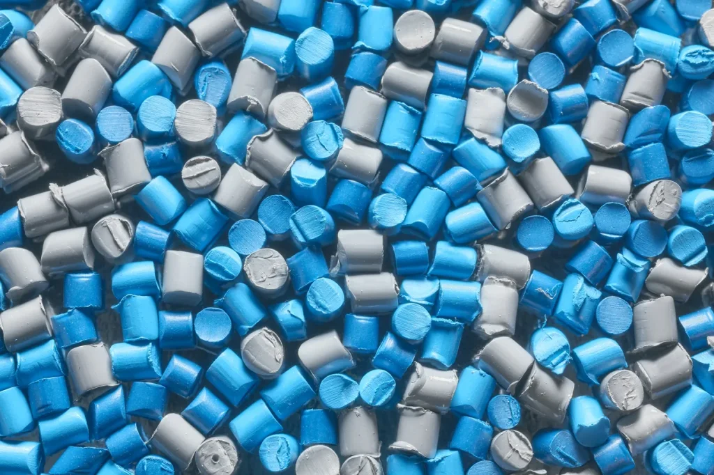 Vista de cerca de pellets pequeños de polímero azul y gris, insumo ideal para fabricar varios tipos de plástico.